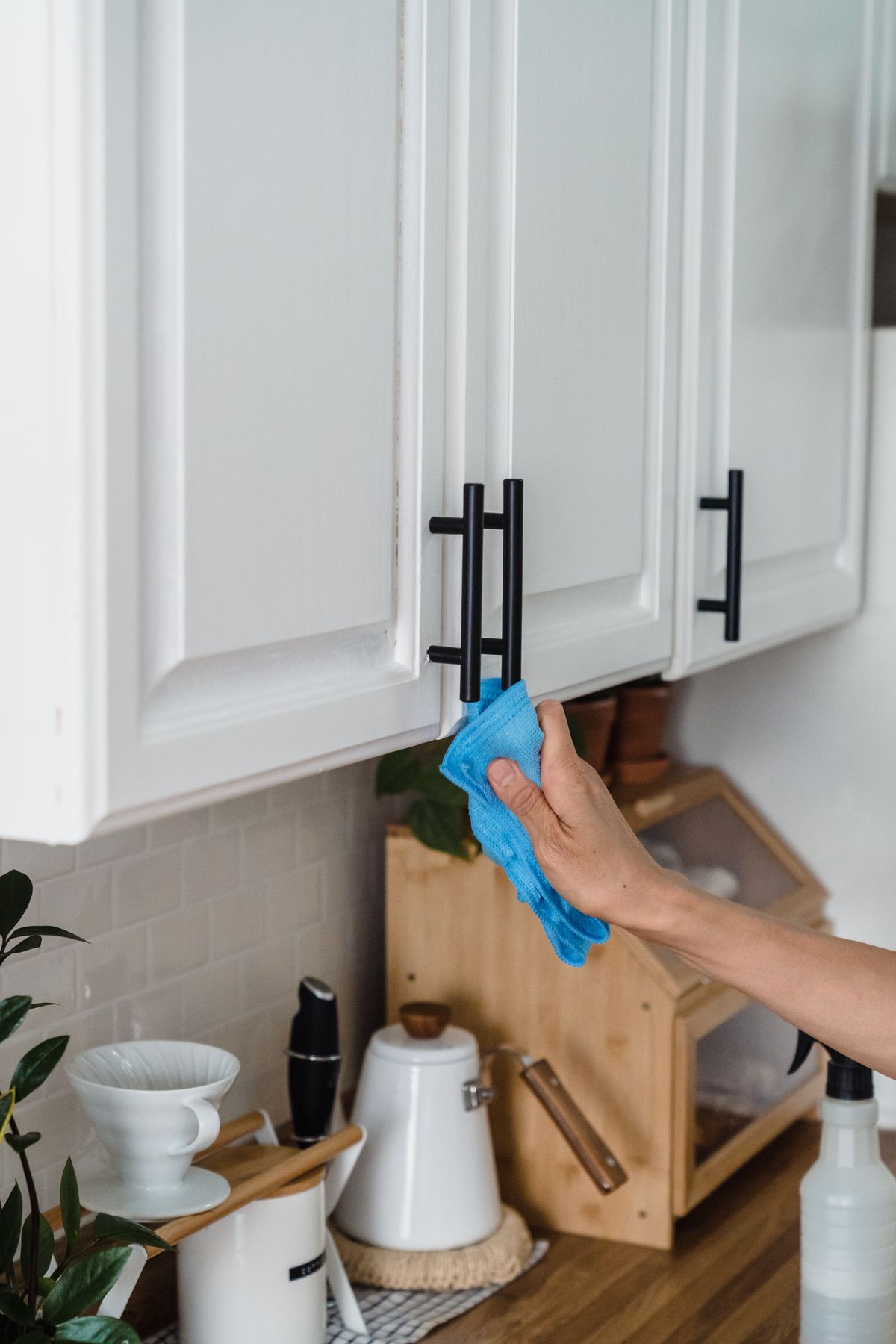 A hand wiping a black kitchen cabinet handle with a blue cloth