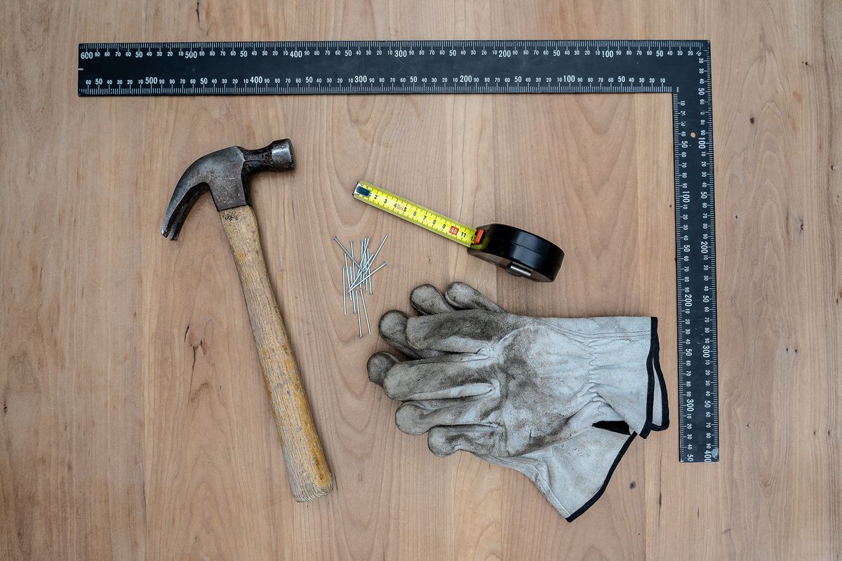 Hammer, work gloves, measuring square, tape measure and nails on a wooden surface
