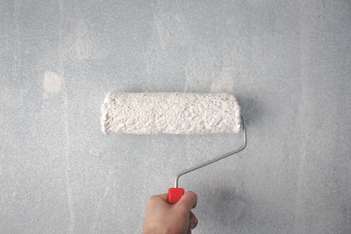 A hand applying white paint to a wall with a roller