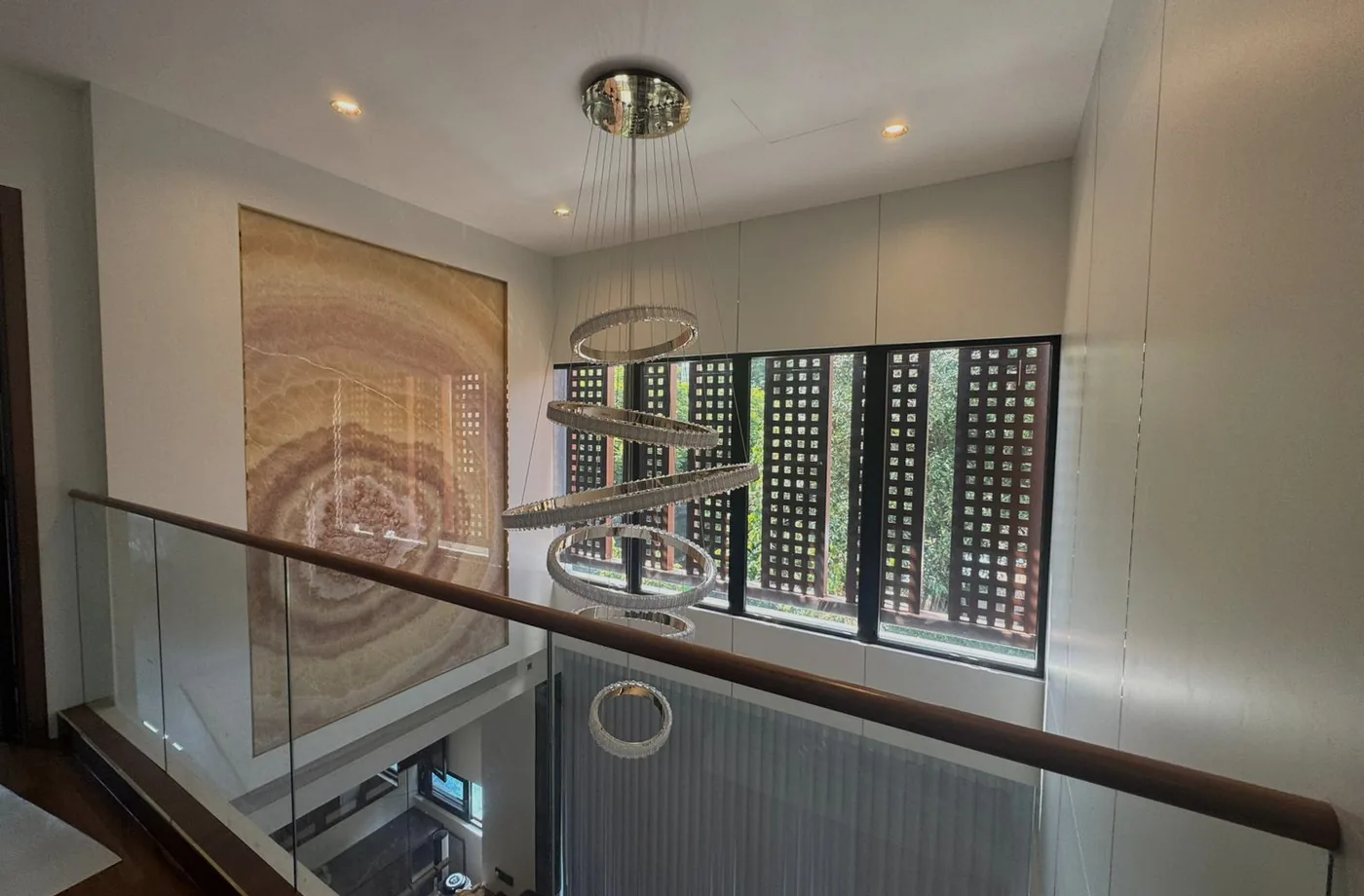 Upper-level view into a double-volume atrium with sculptural ring lighting and full-height stone artwork