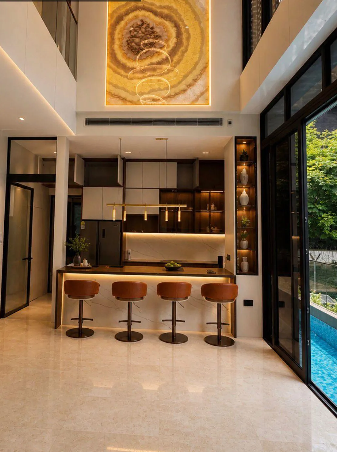 Double-volume kitchen and dining area with a four-seat island, warm joinery and poolside glazing